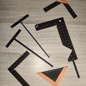 Op de afbeelding: Een set zwarte en oranje plastic tekengereedschappen, waaronder twee T-linialen, twee L-vormige linialen met genummerde markeringen en een driehoekige hoekgeleider. De instrumenten zijn voorzien van duidelijke schaalverdelingen voor metingen.