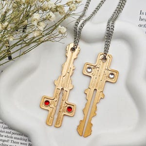 May include: Two gold-coloured key pendant necklaces with silver chains. One key pendant has two red gems, the other has two clear gems. The keys have a circuit board design.
