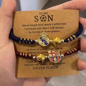 May include: Two football-themed bracelets with blue and maroon braided cords. Each bracelet features a football charm and a team emblem. The card reads "TO MY SON" and includes a message about love and support.