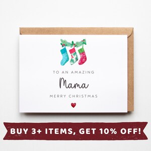 May include: A white Christmas card with a brown envelope, featuring three festive stockings in blue, red, and green. The card reads "TO AN AMAZING Mama MERRY CHRISTMAS" with a red heart. A holiday gift.