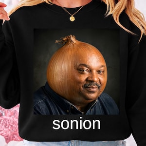 Puede incluir: Sudadera negra con un gráfico humorístico de la cara de un hombre reemplazada por una cebolla. La imagen está enmarcada e incluye la palabra "sonion" en texto blanco en la parte inferior. Prenda casual.