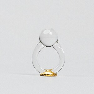 May include: A clear glass ring with a round, clear glass top and a gold base.