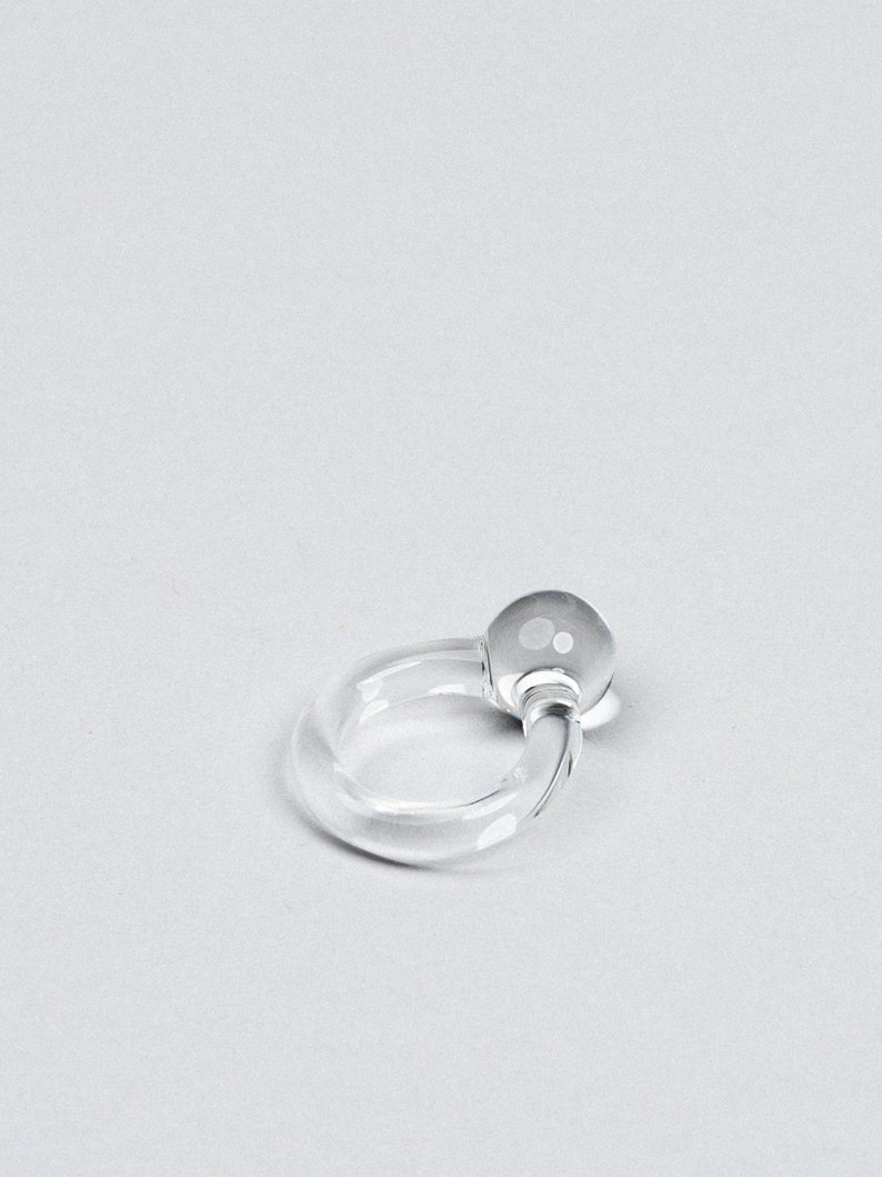 May include: A clear glass ring with a round, clear glass bead on one end.