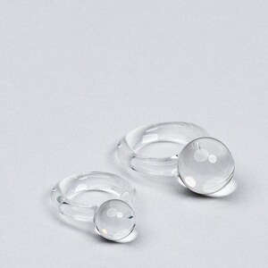 May include: Two clear glass rings with a round orb at the end of each ring.