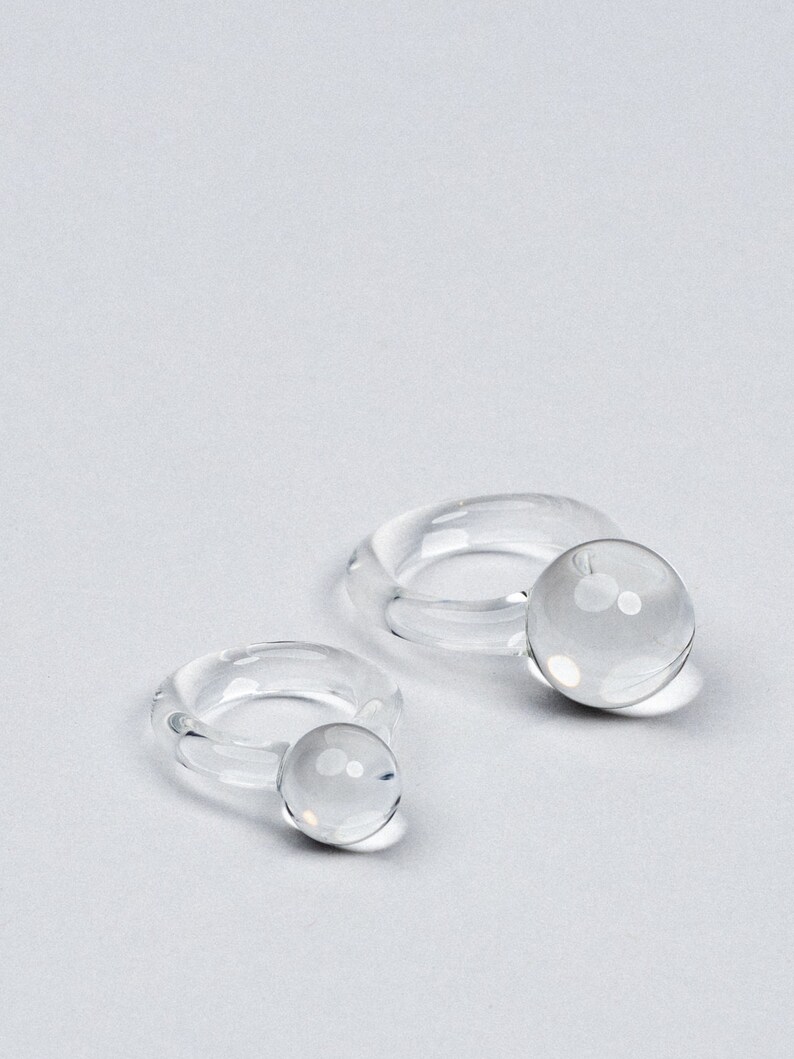 May include: Two clear glass rings with a round orb at the end of each ring.