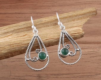 Può includere: Un paio di orecchini pendenti argentati con un design a goccia. Ogni orecchino presenta una pietra verde incastonata in una cornice decorativa di metallo intrecciato. Presentati su una superficie di legno.