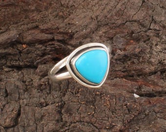May include: A silver ring featuring a triangular, bright turquoise stone. The stone is set within a silver bezel, creating a striking contrast. The ring's band is a simple, elegant design.