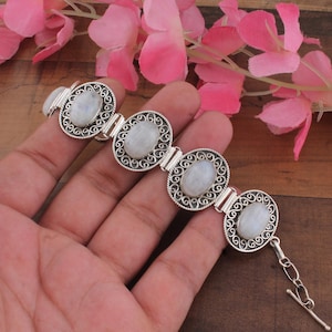 May include: A silver bracelet featuring four oval moonstone cabochons set in intricate filigree frames. The links are connected by small silver bars, and the piece includes a toggle clasp closure with an adjustable chain link extension.