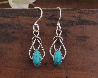 May include: A pair of silver-toned earrings with a turquoise teardrop-shaped stone. The earrings have a unique design with a looped top and a geometric frame around the stone. The turquoise stone has a marbled appearance.