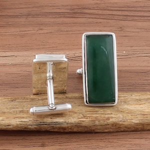 Könnte beinhalten: Ein Paar silberne Manschettenknöpfe mit rechteckigen grünen Jade-Steinen. Die Manschettenknöpfe haben eine polierte Silberoberfläche und einen klassischen T-Bar-Verschluss.