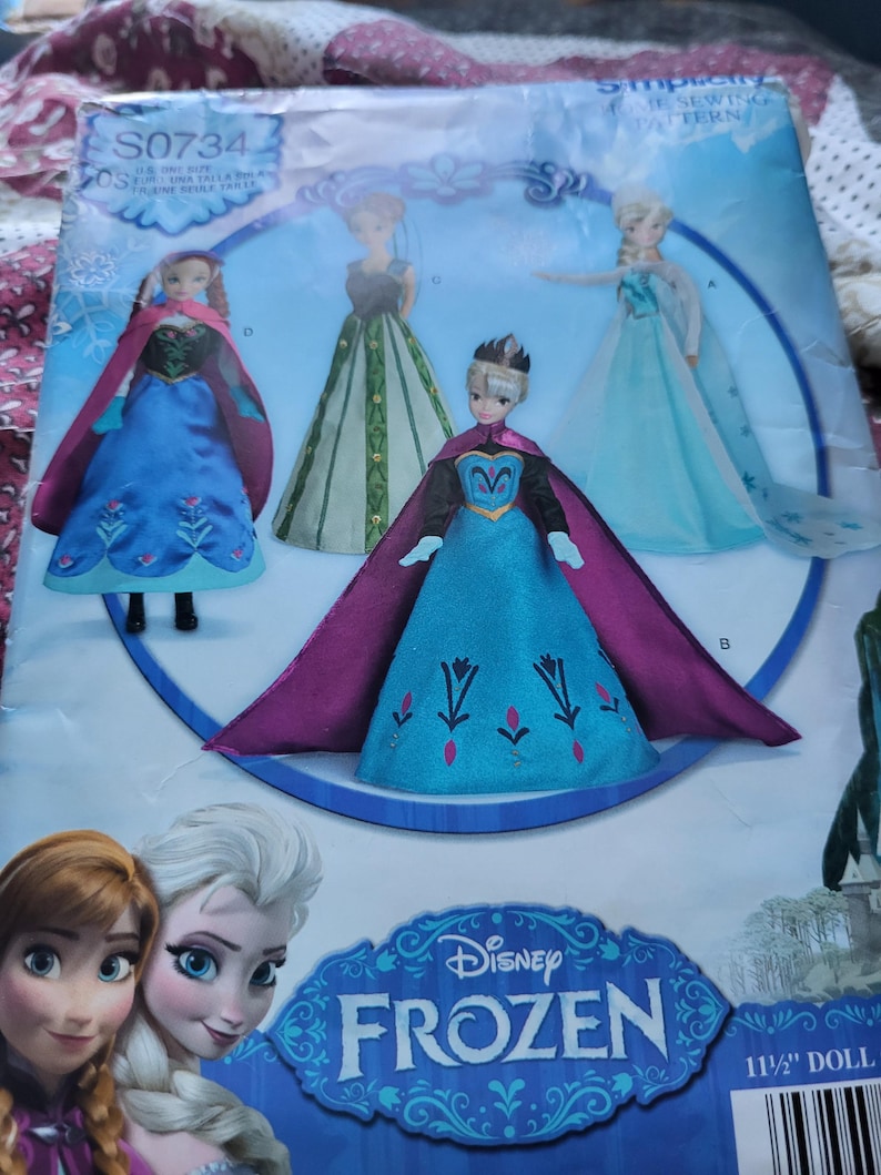 K&ouml;nnte beinhalten: Ein Schnittmuster mit den Charakteren von Disney's Frozen. Das Muster enth&auml;lt Bilder von Elsa- und Anna-Puppen in ihren ikonischen Outfits. Die Verpackung hat das Disney Frozen-Logo und den Text "11 1/2" DOLL".