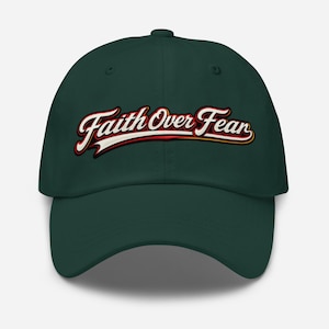 Puede incluir: Una gorra de béisbol de color verde bosque oscuro con el texto Faith Over Fear bordado en una fuente cursiva blanca, roja y negra en el panel frontal. La gorra tiene una corona estructurada, una visera curva y un botón en la parte superior.
