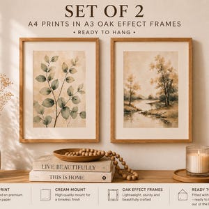 May include: Two framed A4 prints in oak effect frames. One print shows a watercolor of a leafy branch, the other a landscape with trees and a river. The text on the image reads "SET OF 2 A4 PRINTS IN A3 OAK EFFECT FRAMES - READY TO HANG."