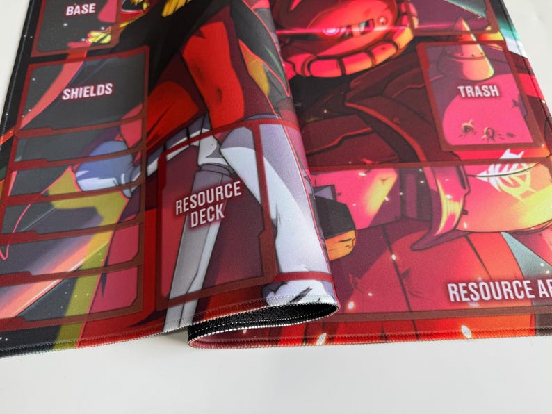 Puede incluir: Alfombrilla de juego roja y negra con una ilustraci&oacute;n detallada de un robot. La alfombrilla presenta secciones etiquetadas para "Base", "Shields", "Resource Deck" y "Trash". Los bordes est&aacute;n cosidos con hilo negro.