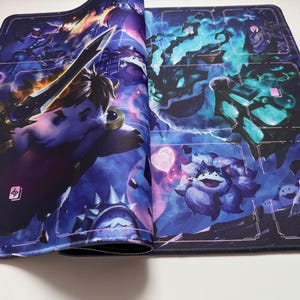 Op de afbeelding: Een gaming muismat met een fantasie-illustratie. De mat heeft een donkerblauwe achtergrond met verschillende personages en elementen, waaronder een zwaardzwaaiend wezen en een pluizig paars personage. Genummerde ruimtes bevinden zich langs de linkerrand.