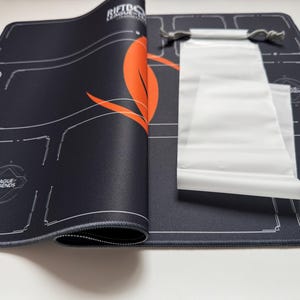 Puede incluir: Alfombrilla de rat&oacute;n para juegos negra con gr&aacute;ficos blancos y naranjas, incluido el texto "RIFTTO", "LEAGUE LEGENDS". Se incluye una bolsa con cord&oacute;n blanca. La alfombrilla tiene un borde cosido y un dise&ntilde;o detallado.