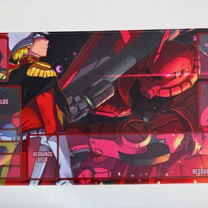 Puede incluir: Alfombrilla de juego rectangular con una vibrante ilustraci&oacute;n de estilo anime. El dise&ntilde;o muestra un personaje con uniforme militar y un robot rojo, con zonas etiquetadas para el juego: Base, Escudos, Mazo, Basura, Mazo de recursos y &Aacute;rea de recursos.