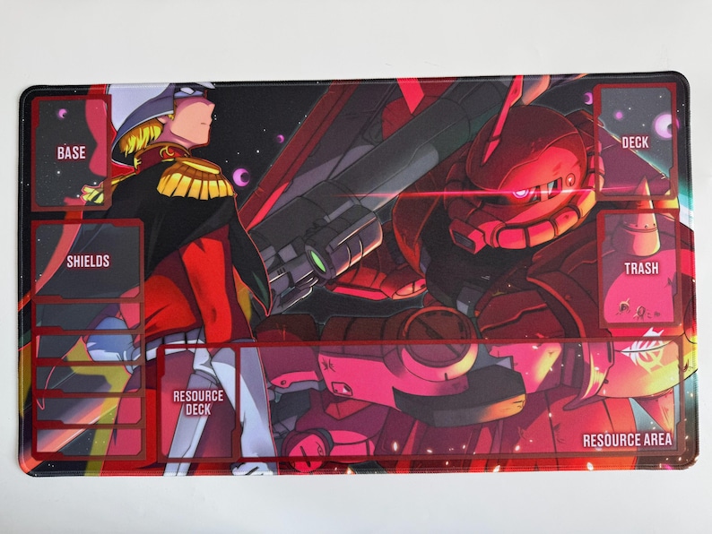 Puede incluir: Alfombrilla de juego rectangular con una vibrante ilustraci&oacute;n de estilo anime. El dise&ntilde;o muestra un personaje con uniforme militar y un robot rojo, con zonas etiquetadas para el juego: Base, Escudos, Mazo, Basura, Mazo de recursos y &Aacute;rea de recursos.