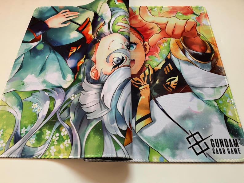 Op de afbeelding: Kleurrijke muismat met anime-stijl illustraties van twee personages. Het ontwerp bevat groene, witte en oranje tinten, met de tekst "GUNDAM CARD GAME" rechtsonder. Het kunstwerk is gedetailleerd.