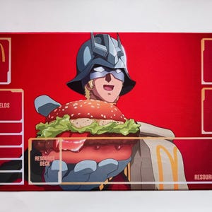 Puede incluir: Una alfombrilla de juego rectangular roja con un personaje de dibujos animados con casco sosteniendo una gran hamburguesa. El logotipo de McDonald's es visible, junto con cuadros de texto etiquetados como "BASE", "SHIELDS", "DECK", "TRASH" y "RESOURCE AREA".