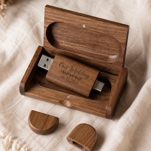 Könnte beinhalten: Ein dunkelbrauner USB-Stick aus Holz mit Metallanschluss, graviert mit dem Text Our Wedding und dem Datum 06.22.2025, liegend in einer offenen passenden Holzschachtel mit zwei kleinen abgenommenen Holzkappen vor dem Behälter.