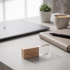 May include: A rectangular USB flash drive featuring a light brown wooden cap and a clear acrylic body. The wooden portion is engraved with the script text "Darling" above the word "memories" in a smaller, clean sans-serif font.