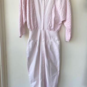 May include: A pink, button-up dress with a textured pattern and a fitted silhouette. The dress has 3/4 sleeves and a round neckline.