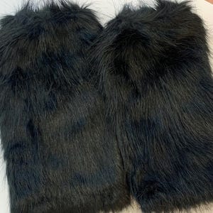 May include: Two sections of black faux fur fabric, featuring long, dense fibres. The fur has a slightly irregular texture, with some fibres upright and others flat. The overall appearance is dark and luxurious.