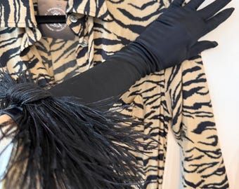 May include: A long black satin glove featuring a dense black feather trim at the wrist, positioned over a tan button-down shirt with a black tiger stripe pattern. The shirt includes a visible circular brand tag near the collar area.