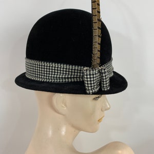 May include: A black felt hat with a black and white checked ribbon and a brown feather accent.