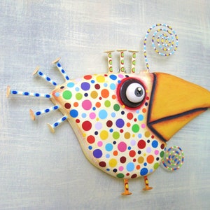 May include: Whimsical bird sculpture with a large yellow beak and a body covered in colorful polka dots. The bird has a large, expressive eye and decorative wire accents. The sculpture is mounted on a light blue background.