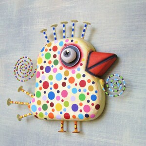 May include: A whimsical, hand-painted bird sculpture with a cream-colored body covered in colorful polka dots. It features a red beak, a large eye, and decorative spiral accents. The bird has six yellow legs and blue-tipped head spikes.