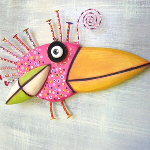 May include: A whimsical pink and orange bird sculpture with a long beak, black eye, and a spiral antenna. The bird is decorated with colorful polka dots and has a green wing.