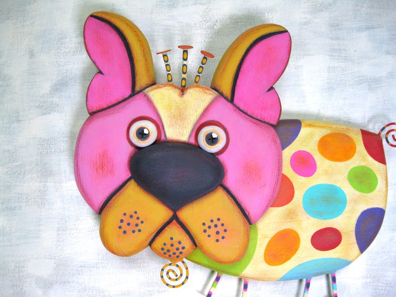 Puede incluir: Escultura de perro de madera caprichosa con cara rosa, detalles amarillos y naranjas y nariz negra. El cuerpo del perro est&aacute; decorado con lunares de colores. La escultura tiene un estilo de arte popular juguet&oacute;n.