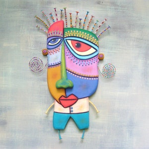 May include: A colorful, abstract face sculpture with a green nose, red lips, and blue, pink, and yellow accents. The sculpture has a whimsical, cartoon-like style and is made of mixed media.