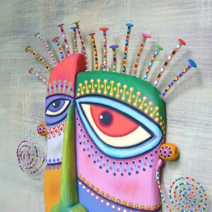 May include: A colorful wooden mask with a whimsical design. The mask features two large eyes, one blue and one red, and a variety of geometric shapes and patterns. The mask is decorated with colorful dots and lines, and has a unique, abstract style.