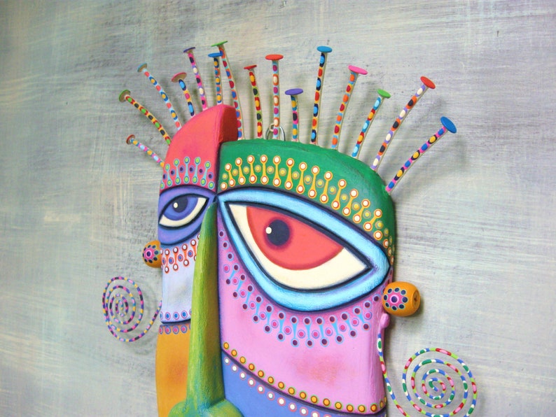 May include: A colorful wooden mask with a whimsical design. The mask features two large eyes, one blue and one red, and a variety of geometric shapes and patterns. The mask is decorated with colorful dots and lines, and has a unique, abstract style.