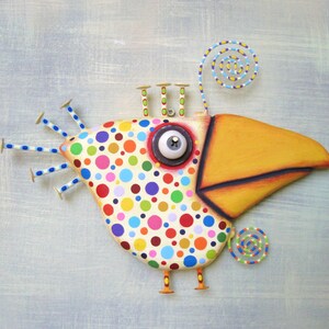 May include: A whimsical, colorful bird sculpture with a large yellow beak and a body covered in polka dots. The bird has a large, expressive eye and nail-like accents. The sculpture is a unique piece of art.