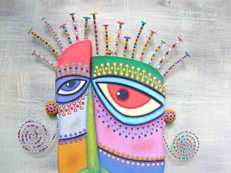 May include: A colorful, abstract mask with a green, pink, blue, and orange face. The mask has two large eyes with white pupils and a spiky, multi-colored hairpiece.