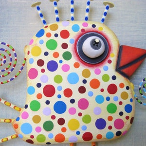 May include: A whimsical, handcrafted bird sculpture with a cream-colored body adorned with colorful polka dots. It features a large eye, a red beak, and decorative spirals. The bird has multiple antennae and legs, all with yellow and blue accents.