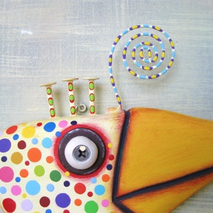May include: A whimsical, colorful fish sculpture with a large yellow beak and a spiral accent. The fish's body is cream-colored with vibrant polka dots in various colors. It has a large, round eye and three small, decorative posts.