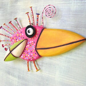 May include: A whimsical pink and orange bird sculpture with a large beak, black eye, and a spiral on top. The bird is decorated with colorful polka dots and has a green and white beak.
