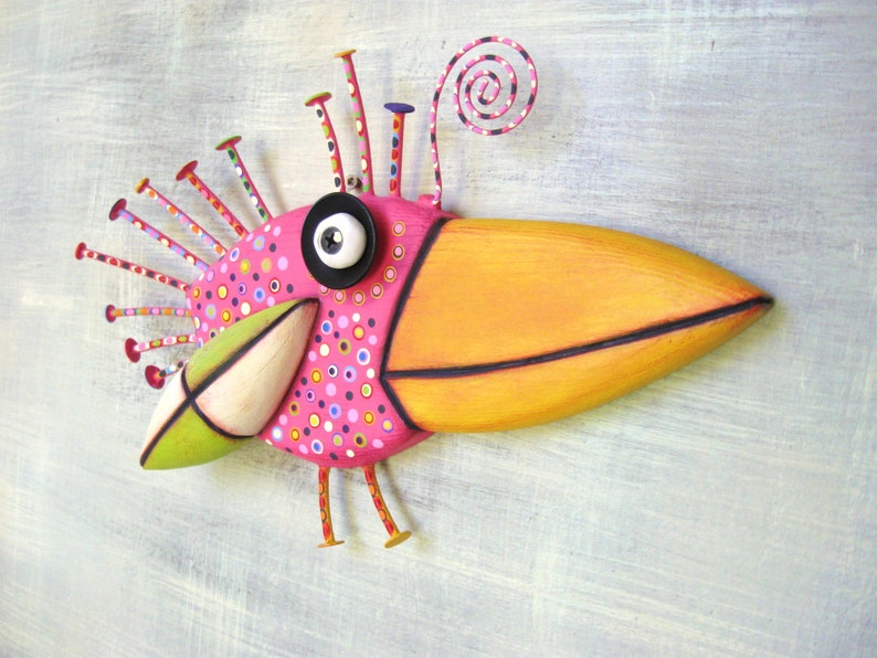 May include: A whimsical pink and orange bird sculpture with a large beak, black eye, and a spiral on top. The bird is decorated with colorful polka dots and has a green and white beak.