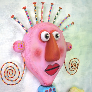 May include: A pink, whimsical face with large eyes, a long orange nose, and red lips. The face has a colourful, spiky hairdo and spiral-shaped earrings.