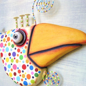 May include: A whimsical, colorful bird sculpture with a large yellow beak and a body covered in polka dots. The bird has a large, round eye and decorative metal accents. The sculpture is painted in bright, cheerful colors, making it a fun piece of art.