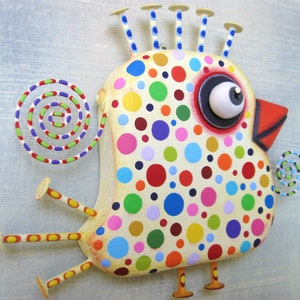 May include: A whimsical, colorful bird sculpture with a cream-colored body covered in multi-colored polka dots. It has a large eye, a red beak, and decorative spirals. The bird has stick-like legs and a crown of small posts.