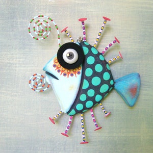 May include: A whimsical, hand-painted metal fish wall art piece. The fish features a light blue body with a black and teal polka-dotted section. It has a large, round eye, a blue tail, and colorful accents.