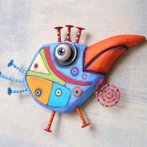 May include: A whimsical, colorful bird sculpture with a blue body, orange beak, and red accents. The bird has a large eye, three antennae, and decorative legs. The design incorporates geometric shapes and a spiral tail, creating a playful, artistic aesthetic.