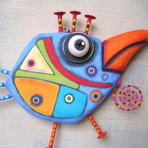 May include: A whimsical, colorful bird sculpture with a blue body, orange beak, and red accents. The bird has a large eye, decorative legs, and a spiral tail. The artwork is a unique, handcrafted piece.
