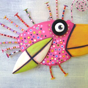 May include: A whimsical pink bird with a long orange beak, green and white wings, and a black button eye. The bird has a colorful, polka-dotted body and a spiral antenna on its head.